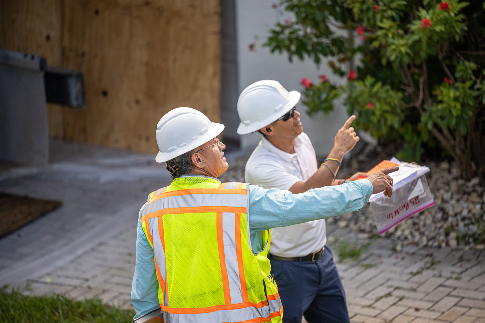 Two Campany supervisors in hard hats and vests reviewing paperwork and pointing at a roof during an assessment