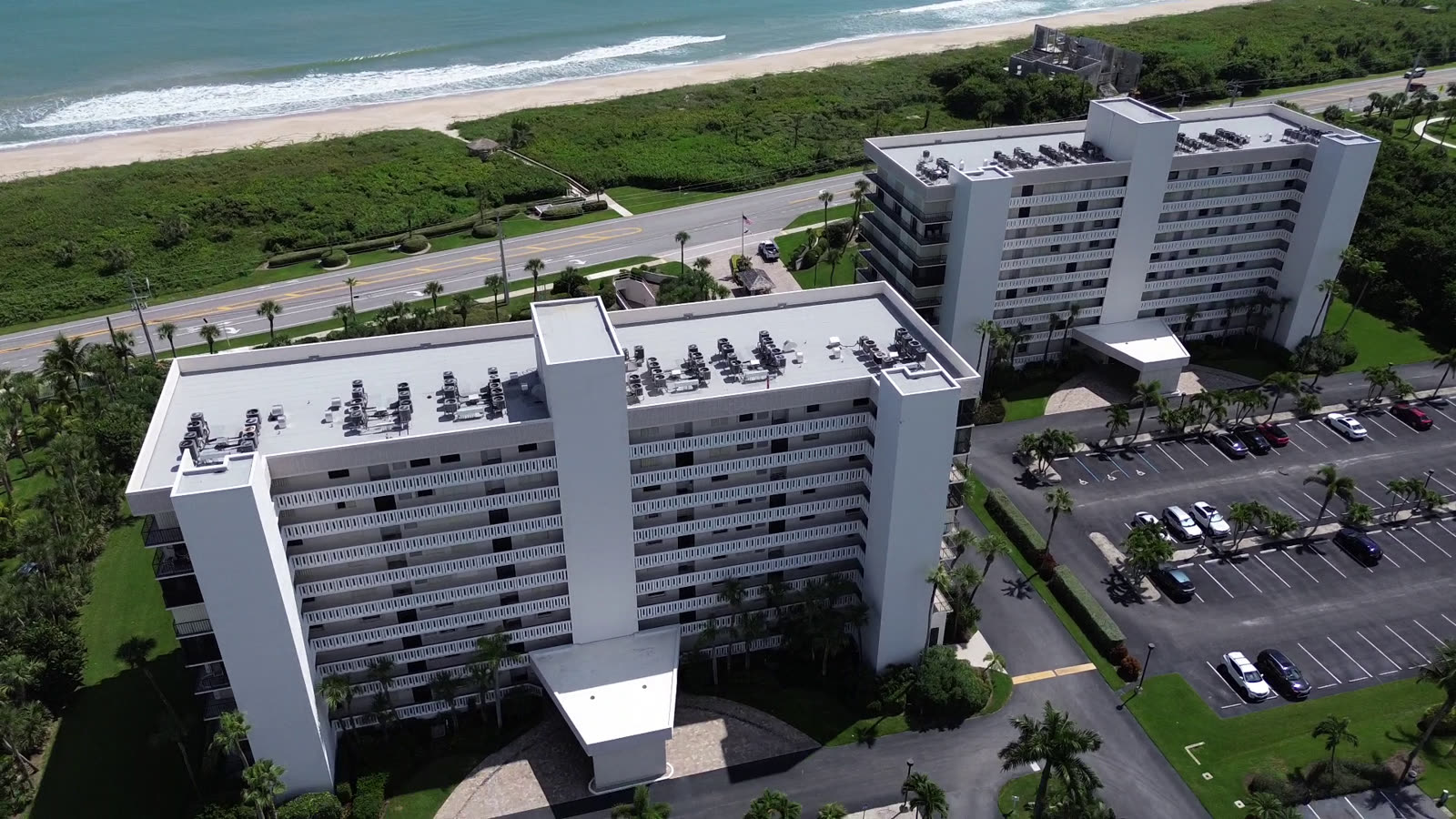 Drone still of twin beachfront condominium towers with new white roofs beside the dune line
